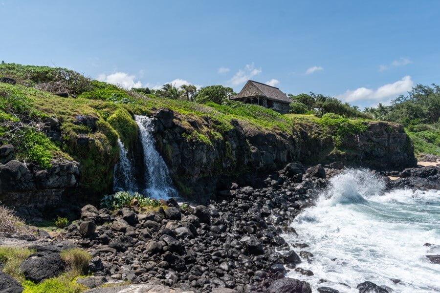 a waterfall flowing into the ocean with a small brick building in the background at seneville waterfall