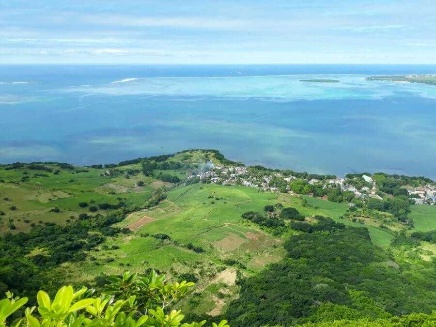 aerial view of a green field bordered by the ocean from the top of lion mountain