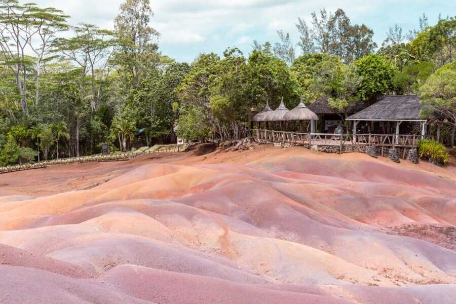 colorful sand dunes with small wooden huts in the distance at Chamarel Seven Colored Earth