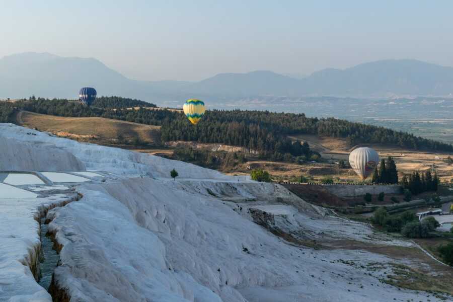 Hot air balloons floating above the Pamukkale travertines with mountains in the backdrop