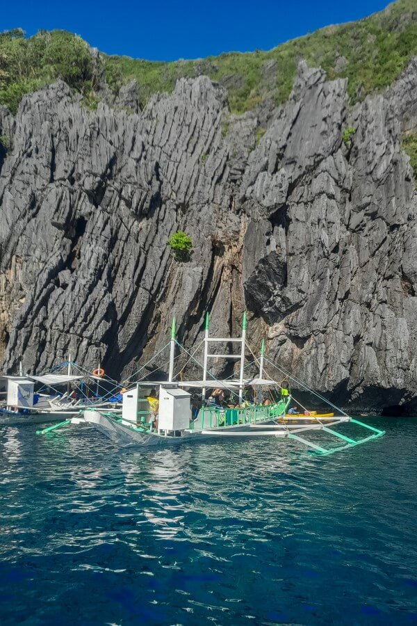 a white an green boat with a limestone cliff in the backdrop in el nido philippines
