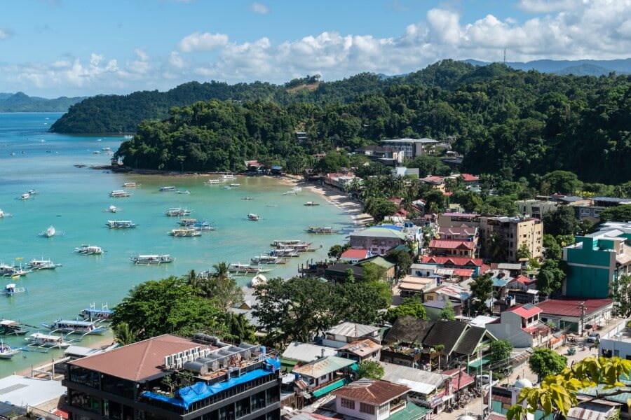 a bird's eye view of el nido beach covered by boats and surrounded by mountains