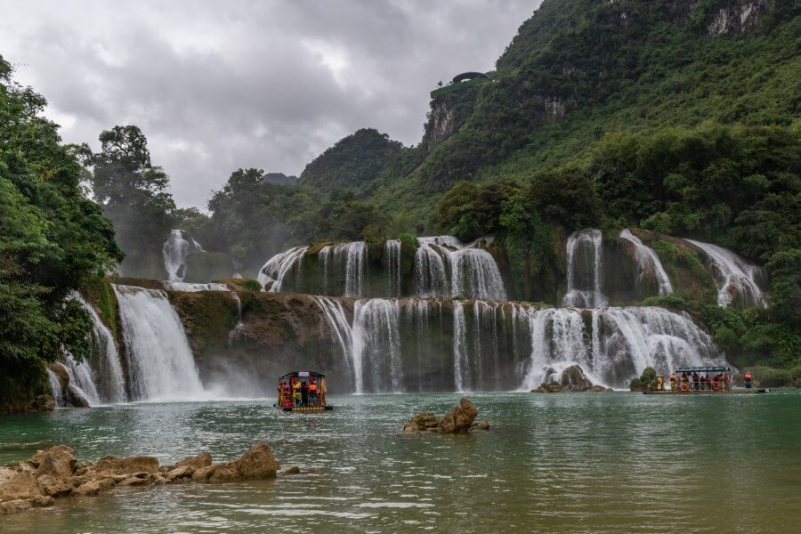 a boat cruising toward a multi-tier waterfall at ban gioc vietnam