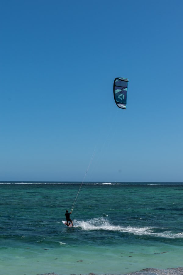 a man dressed in black t-shirt and shorts kitesurfing at the beach