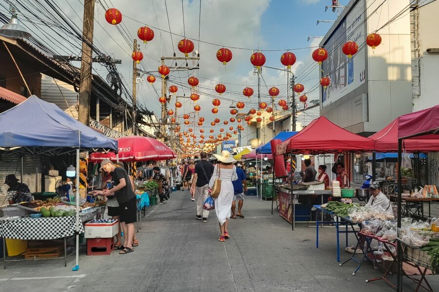 people walking along a road surrounded by stalls selling food and souvenirs